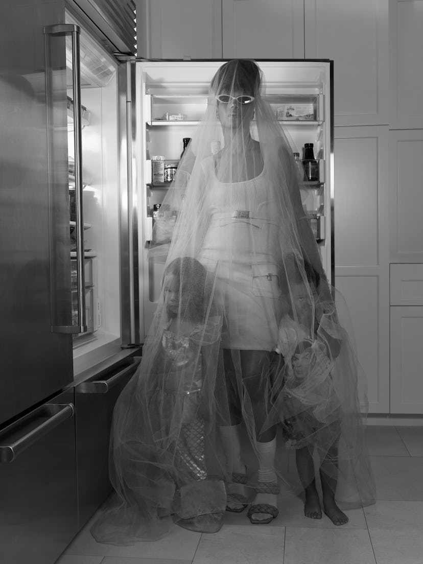 The musician Santigold wearing a bridal veil that covers two small children at her side, standing in...