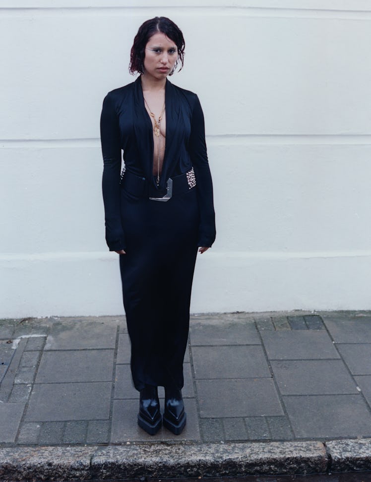 Raye wears a Versace dress, earrings, necklace, belt, and boots.